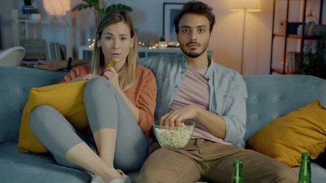 Portrait of two people couple watching scary movie on TV hugging eating popcorn in dark apartment. Relationship and entertainment concept.