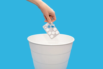A hand throws pills into a trash can on a blue background. The concept of drug withdrawal or...