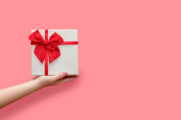 White gift box in a human hand on a pink background. Beautiful gift box decorated with ribbon and bow. The concept of giving gifts for birthday or traditional holidays. Free space for text