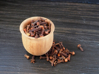 Wooden bowl with dried cloves (Syzygium aromaticum) isolated on black wooden background. Close-up
