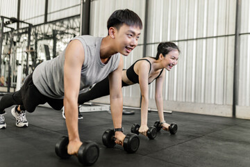 Fototapeta na wymiar exercise concept The female and male members of the gym doing the basic renegade row posture with dumbbells while looing at each other’s face