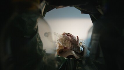 Woman putting empty plastic bottle in recycling bin in the kitchen. Bottom view from the trash bin....
