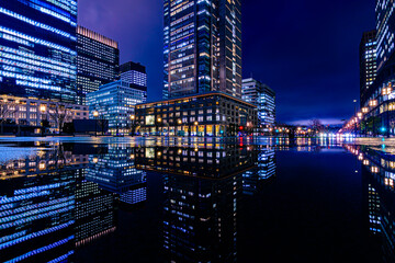 Obraz premium Night city view of business buildings around the Marunouchi side of Tokyo Station after rain. Reflection photo with beautiful specular reflection.