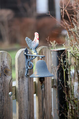 Eine Glocke mit einem Hahn an einem Gartentor.
