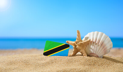 Tropical beach with seashells and Tanzania flag. The concept of a paradise vacation on the beaches of Tanzania and Zanzibar islands.