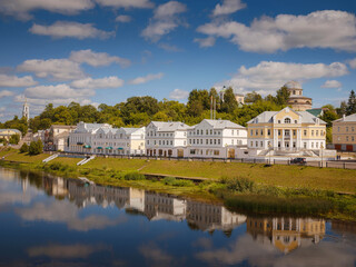 Fototapeta na wymiar summer travel to Russia, Torzhok city, Tver region. View on old buildings at the embankment from the bridge across the Tvertsa river. Rural landscape
