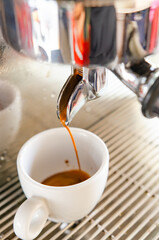 Espresso from a coffee machine pouring into a white cup of coffee.