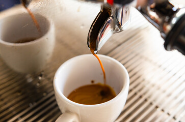 Espresso from a coffee machine pouring into a white cup of coffee.