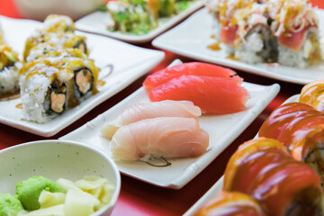 Closeup of sushi with various rolls, yellowtail nigiri, tuna nigiri, wasabi, edamame.