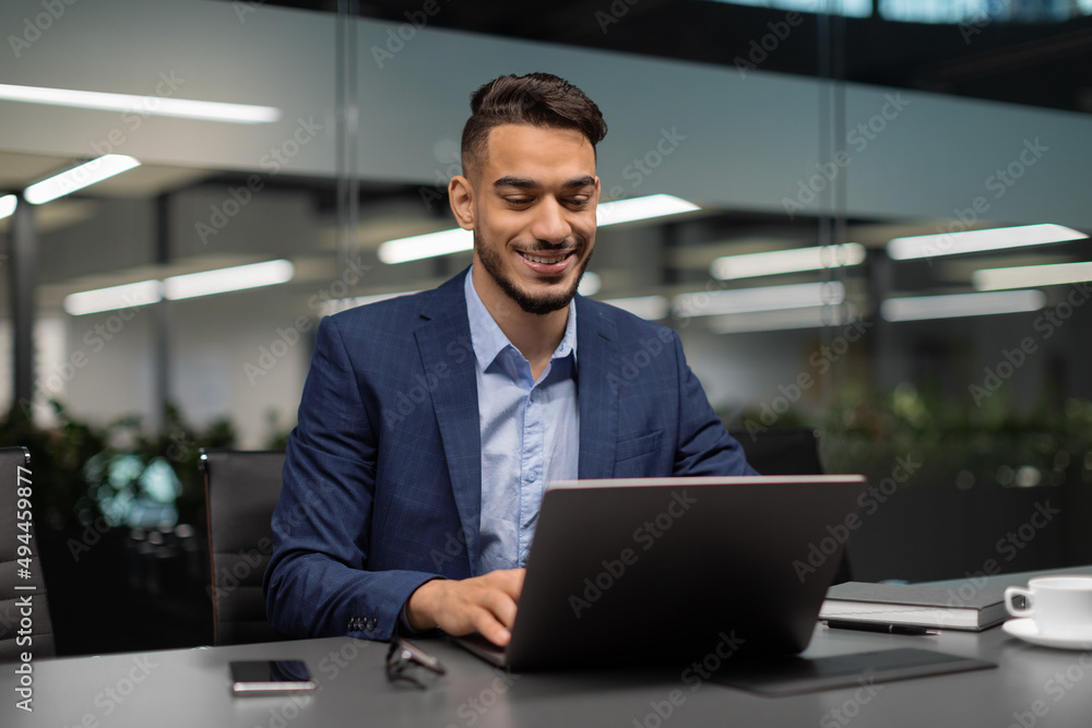 Poster smiling middle eastern businessman typing on computer at office