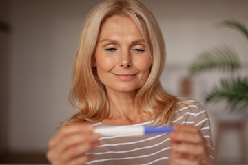 Senior woman smiling with a positive pregnancy test. Artificial insemination, infertility.