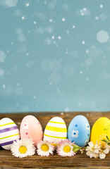 Easter card, colored eggs with flowers on a wooden table, blue background and copy space. Blurred lights on a blue background, Easter eggs and small daisies.