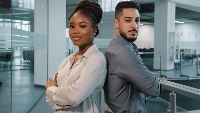 Two confident workers multiracial diverse business co-workers colleagues partners indian arab man and african woman lawyers businesspeople standing in office crossing arms posing looking at camera