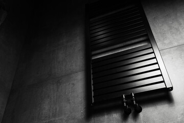 Photo of black matte heated towel rail, in the bathroom with dark grey walls.