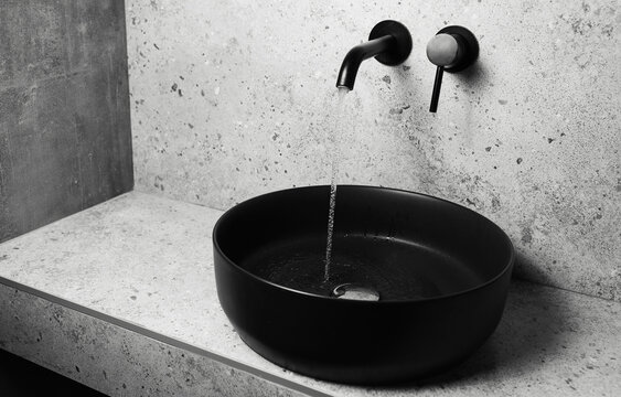 Photo of bathroom details: black sink and faucet with flowing water.  Close-up.