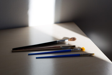 Selective focus view of series of artist paint brushes set on corner of pale work table in ray of light