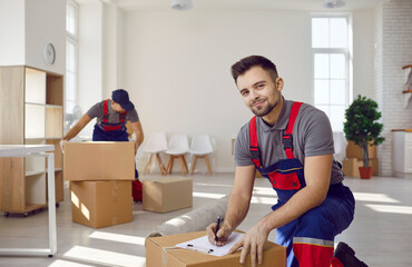 Moving service workers pack cardboard boxes and checking list in client's apartment. Portrait of...