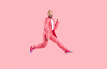 Happy excited funny young man in suit and sneakers having fun jumping on pink background. Cheerful...