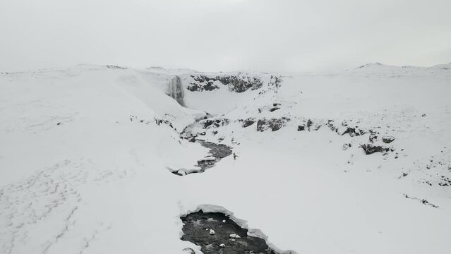 Aerial follow shot of man hiking on snowy mountains towards Sv&ouml;&eth;ufoss Waterfall in Sn&aelig;fellsnes peninsula,iceland