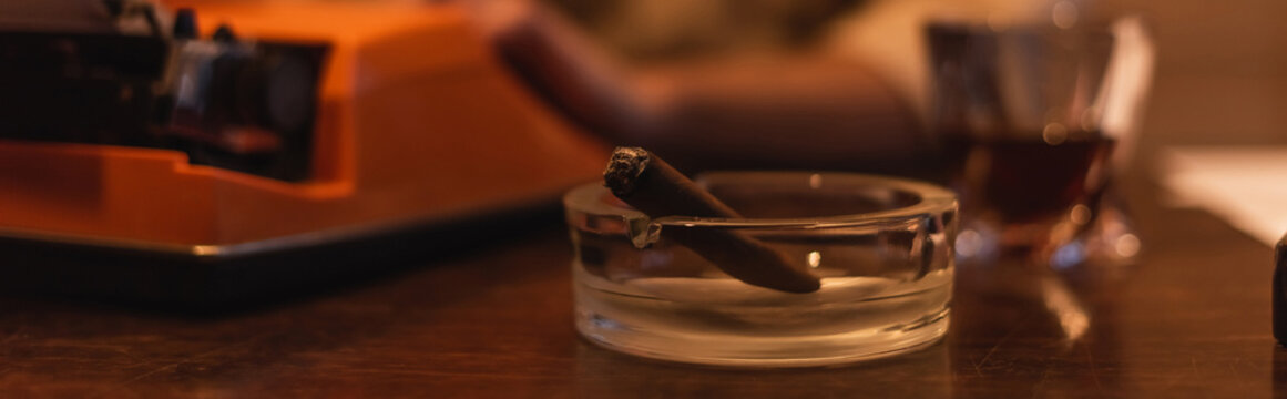ashtray with cigar near typewriter machine on desk, banner.