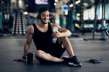 Workout App. Happy Arab Male Athlete Using Smartphone After Training In Gym