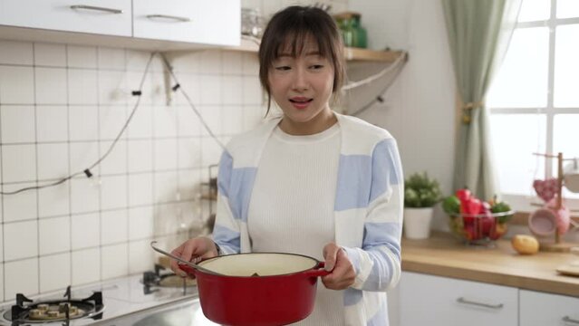 slow motion of cheerful asian mom preparing food for husband and daughter. she serves a pot of soup on dining table and enjoys the delicious smell with her hand fanning