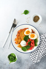 Breakfast. Potatoes latkes with sour cream, spinach salad, tomatoes and boiled eggs on light background. Delicious food for breakfast. Top view.