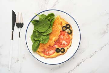 Omelette with tomatoes, black olives, cottage cheese and green spinach herbs on white plate on grey concrete background. Delicious breakfast. Healthy breakfast food. Top view.