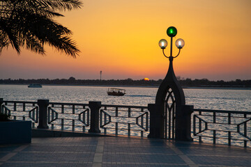 Enchanting sunset in Abu Dhabi Corniche with silhouetted traditional boat passing by