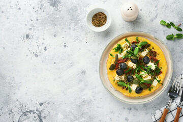Scrambled eggs. Light, Fluffy and Buttery Scrambled Eggs with feta cheese, sun-dried tomatoes and black olives on plate over white stone background. Delicious breakfast. Top view, flat lay.