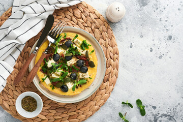 Scrambled eggs. Light, Fluffy and Buttery Scrambled Eggs with feta cheese, sun-dried tomatoes and black olives on plate over white stone background. Delicious breakfast. Top view, flat lay.