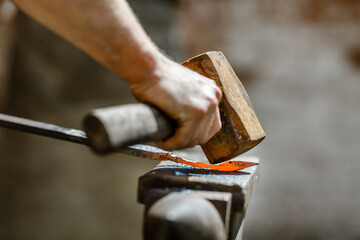 Blacksmith working metal with hammer on the anvil in the forge.