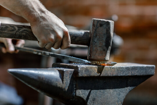 Blacksmith working metal with hammer on the anvil in the forge.