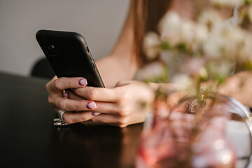 Young female hands hold a phone, freelancer works in a coffee shop, close-up