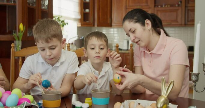 mother and her two sons paint Easter eggs