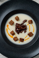 Creamy soup with croutons and sun dried tomatoes, top view in black matt bowl