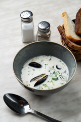 A small portion of milk clam chowder with mussels and dill, bread basket aside, light marble table