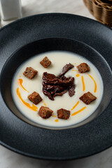 Creamy soup with croutons and sun dried tomatoes, top view in black matt bowl