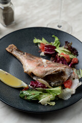 Plain roasted pike perch with lemon and salad on matt black plate, close up for menu