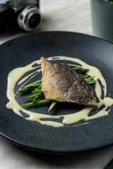 Whole headless roasted dorado with asparagus, seasoned with mustard sauce, black matt dish, top view