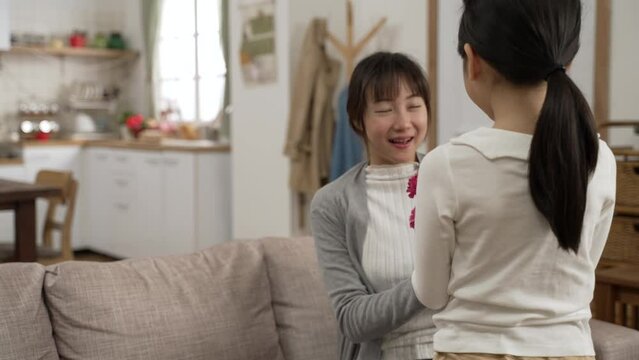 rear view of asian little girl giving mother carnation bouquet on mother's day at home. she hides flower on back and walks up to her smiling mom