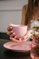 Woman's hand holds a pink mug with coffee, breakfast in a coffee shop