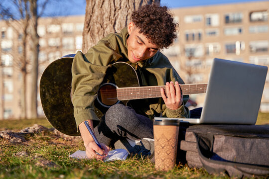 self-taught young man playing and learning to play the guitar with the laptop. teenager composing a song.