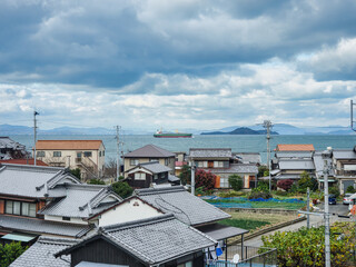 Fototapeta na wymiar 海岸の民家越しに瀬戸内海を航行中のタンカーが見える風景