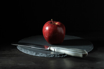 Closeup of a red apple half in a shadow and a knife on a slate plate