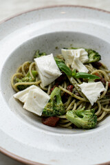 Pesto green spaghetti with broccoli and young cheese chunks, clay restaurant bowl, high angle menu photo