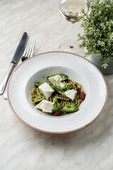 Pesto pasta with broccoli and goat cheese chunks, rustic restaurant bowl, marble table