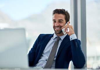 Lets talk business. Shot of a young corporate businessman sitting at a desk in front of a laptop and talking on a cellphone.