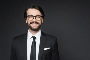 cheerful businessman with mustache in glasses smiling on dark grey.