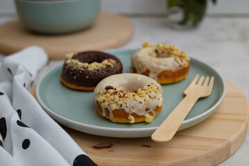 Plate of glazed donuts with crushed nuts and a wooden fork on a trivet